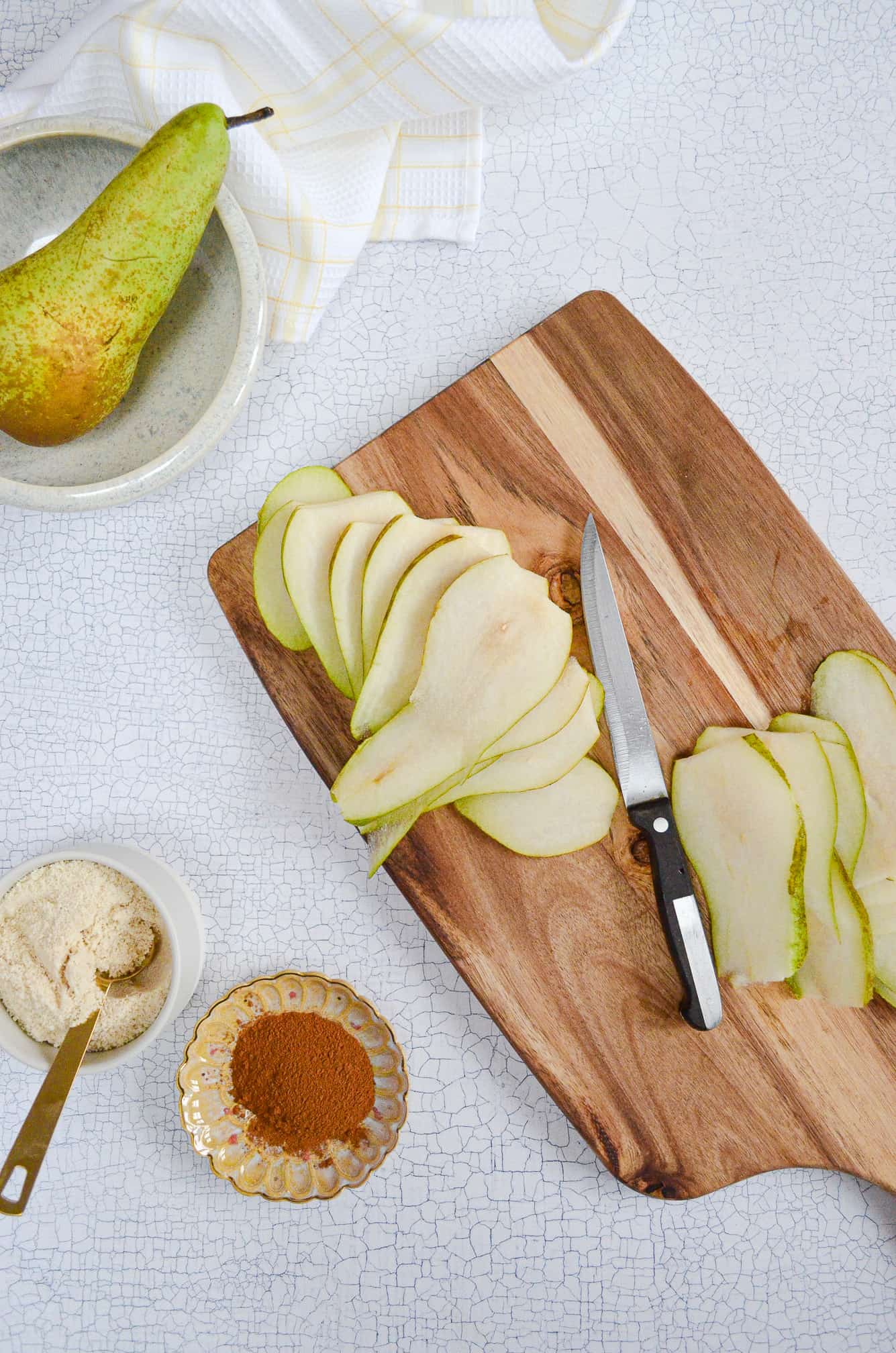 sliced pears on a wooden board with bowls of ingredients to the lefthand side