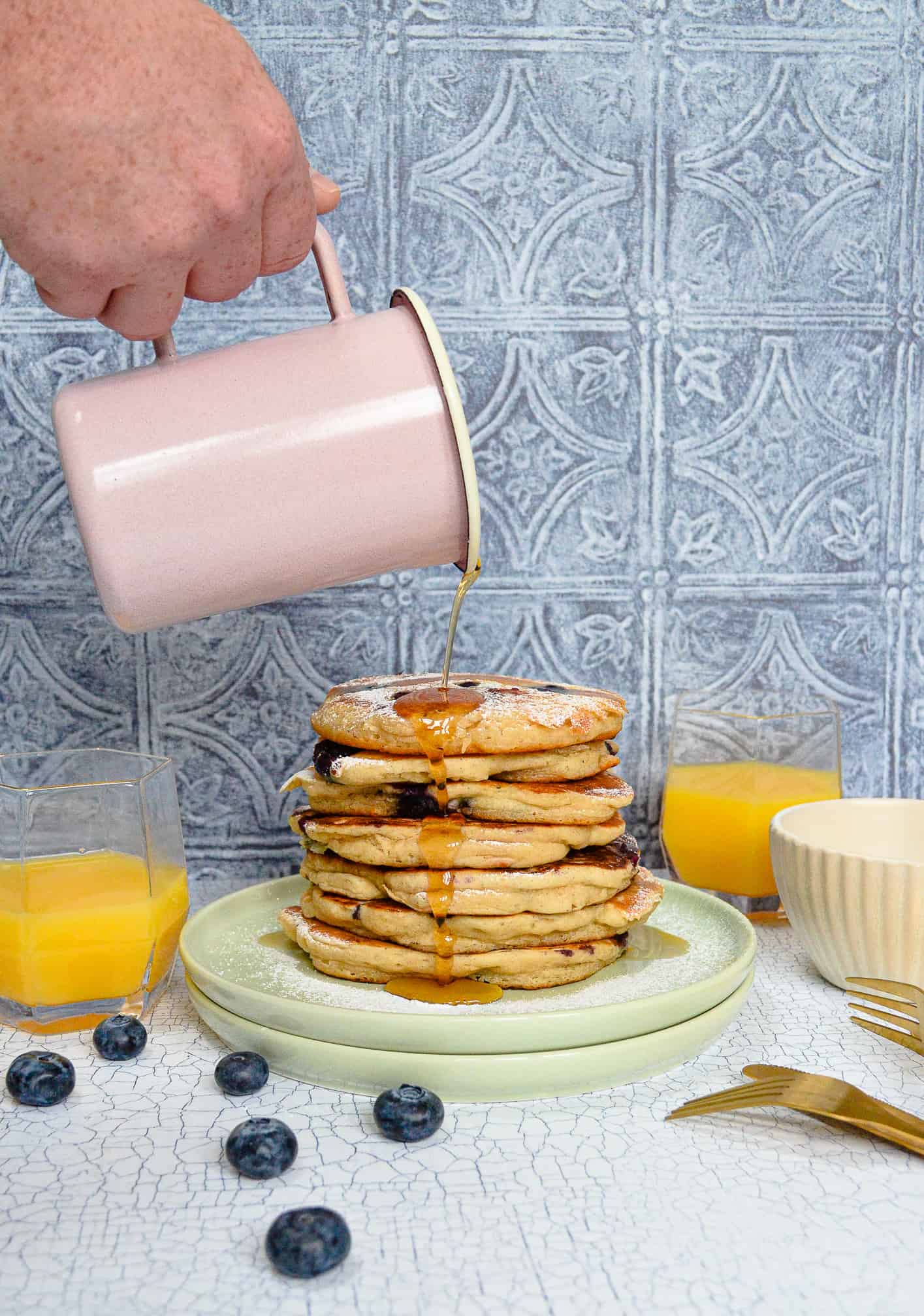 quick & easy vegan blueberry pancakes. Pictured pouring maple syrup over stack of pancakes. 